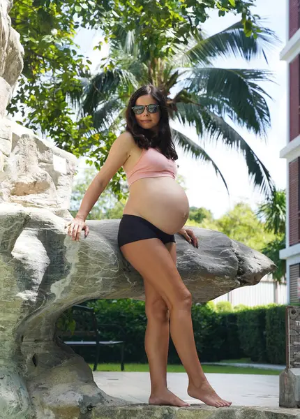 Hamile bir kadın zarif bir şekilde güzel bir şelale kayasının önünde duruyor..