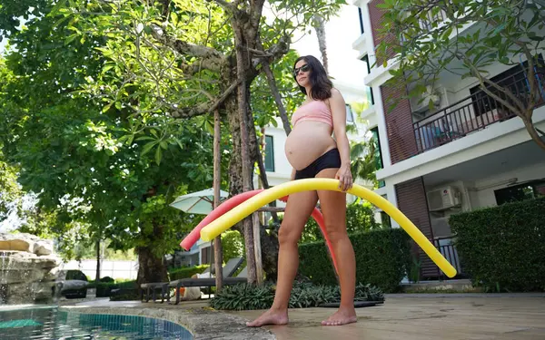 Bilardo oynamak üzere olan hamile genç kadın köpüklü makarnayla havuzda egzersiz yapacak..