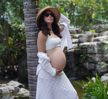 Hamile bir kadın zarif bir şekilde güzel bir şelale kayasının önünde duruyor..