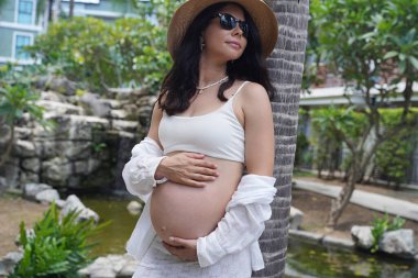 Hamile bir kadın zarif bir şekilde güzel bir şelale kayasının önünde duruyor..