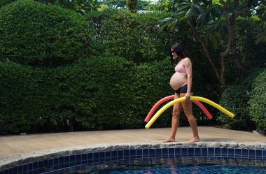 Bilardo oynamak üzere olan hamile genç kadın köpüklü makarnayla havuzda egzersiz yapacak..