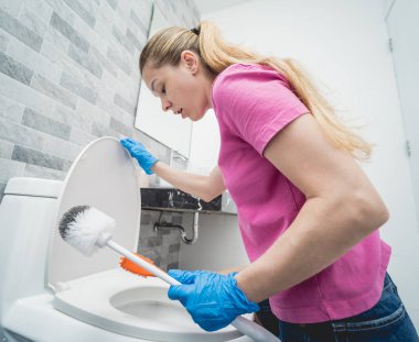 Genç ev hanımı banyodaki klozeti özenle temizler ve yıkar..