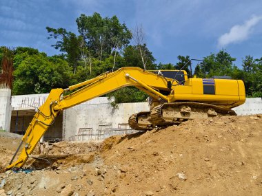 Büyük, sarı bir kazıcı şu anda büyük bir toprak yığınının üzerinde konumlanmış durumda..