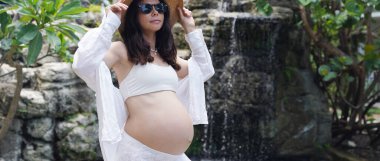 Hamile bir kadın zarif bir şekilde güzel bir şelale kayasının önünde duruyor..