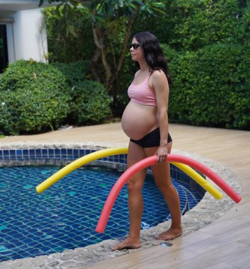 Bilardo oynamak üzere olan hamile genç kadın köpüklü makarnayla havuzda egzersiz yapacak..