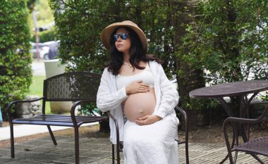 Hamile bir kadın zarif bir şekilde güzel bir şelale kayasının önünde oturuyor..