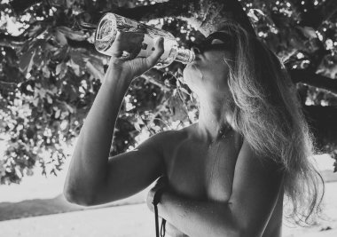 Bikinili bir kadın ıssız bir sahilde biberondan içiyor..