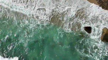 Dev okyanus dalgaları, büyük kaya taşlarıyla boş kumsallara çarpıp köpürüyor.. 