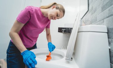 Genç ev hanımı banyodaki klozeti özenle temizler ve yıkar..