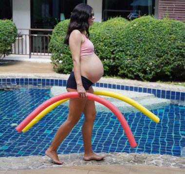 Bilardo oynamak üzere olan hamile genç kadın köpüklü makarnayla havuzda egzersiz yapacak..