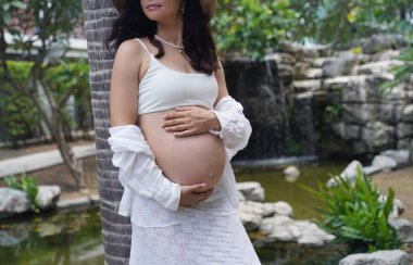 Hamile bir kadın zarif bir şekilde güzel bir şelale kayasının önünde duruyor..