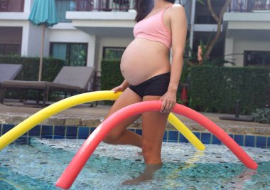 Bilardo oynamak üzere olan hamile genç kadın köpüklü makarnayla havuzda egzersiz yapacak..