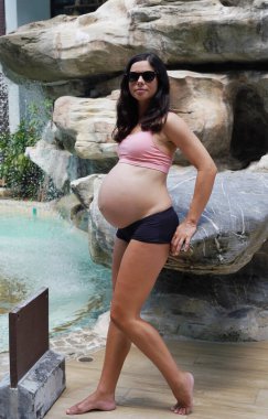 Hamile bir kadın zarif bir şekilde güzel bir şelale kayasının önünde duruyor..