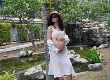 Hamile bir kadın zarif bir şekilde güzel bir şelale kayasının önünde duruyor..