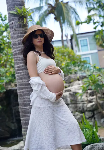 Hamile bir kadın zarif bir şekilde güzel bir şelale kayasının önünde duruyor..