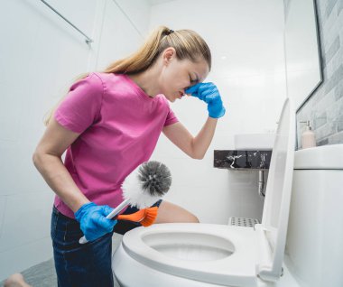 Genç ev hanımı banyodaki klozeti özenle temizler ve yıkar..