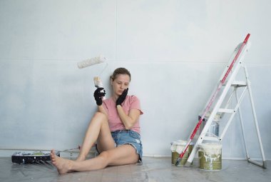 Merdiven kullanarak duvarları silindirle boyayan genç bir kadın..