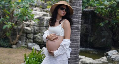 Hamile bir kadın zarif bir şekilde güzel bir şelale kayasının önünde duruyor..