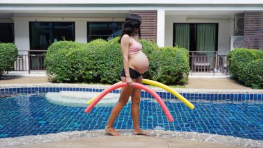 Bilardo oynamak üzere olan hamile genç kadın köpüklü makarnayla havuzda egzersiz yapacak..
