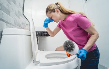 Genç ev hanımı banyodaki klozeti özenle temizler ve yıkar..