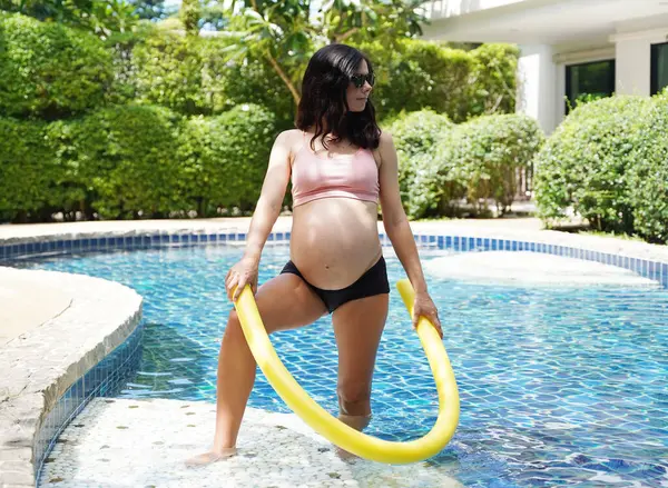 Bilardo oynamak üzere olan hamile genç kadın köpüklü makarnayla havuzda egzersiz yapacak..