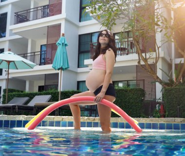 Bilardo oynamak üzere olan hamile genç kadın köpüklü makarnayla havuzda egzersiz yapacak..