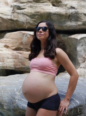 Hamile bir kadın zarif bir şekilde güzel bir şelale kayasının önünde duruyor..