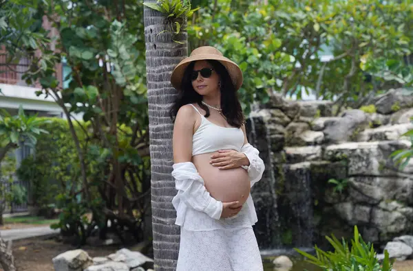 Hamile bir kadın zarif bir şekilde güzel bir şelale kayasının önünde duruyor..