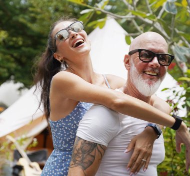 Bir erkek ve bir kadın büyük bir çadırın önünde sarılıp eğleniyorlar.