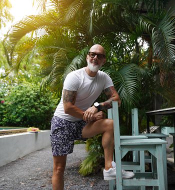 Sakallı bir adam parkta bir masanın yanında poz veriyor.