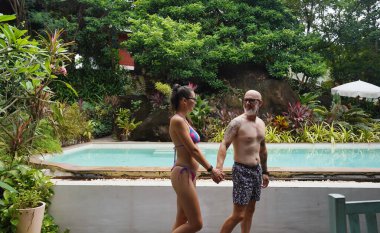 Bir adam ve bir kadın güzel bir havuzun önünde neşeyle yürüyorlar..