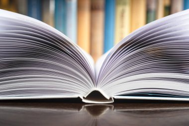 Arkaplanda bulanık kütüphane rafı olan açık kitabın kapatılması