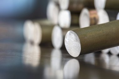 Atölyedeki metal bir yüzey üzerindeki çelik çubuk, fabrikanın bulanık arka planında parçalardan oluşan bir yığın.