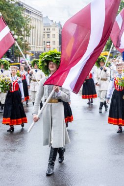 RIGA, LATVIA, 2 Temmuz 2023: Letonya 'da düzenlenen Letonya Şarkı ve Dans Festivali' nin açılış töreninde meşe yaprağı ile süslenmiş neşeli bir katılımcı gururla Letonya bayrağını taşıyor.