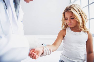 Kolunu sevimli küçük kız arıyor. Çocuk doktoru onun doktor ofisinde oturan bir enjeksiyon yapıyor