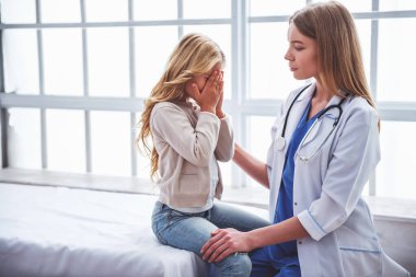 Sakinleştirici sevimli küçük kız, ağlayan, doktor ofisinde oturan güzel genç çocuk doktoru olduğunu