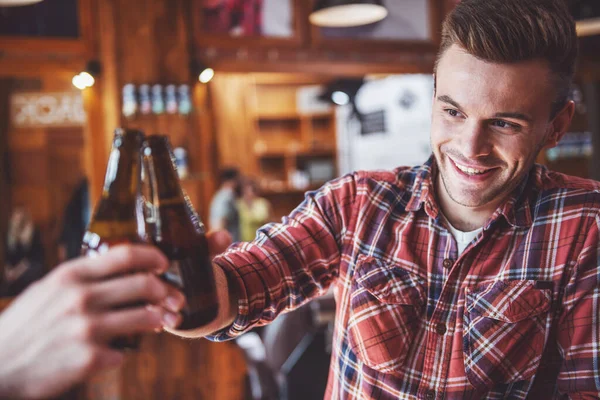 Przystojny Młody Człowiek Jest Brzęk Butelek Piwa Uśmiechając Się Siedząc — Zdjęcie stockowe