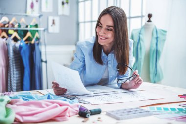 Güzel genç tasarımcı, bazı kroki inceleyerek ve dressmaking stüdyoda çalışırken gülümseyen, bir kağıt parçası tutuyor