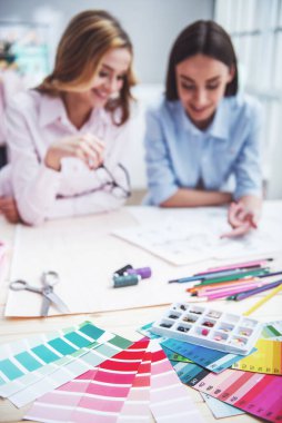 Palet, iplik ve tablo, arka planda Genç tasarımcılar skeçler tartışmak ve gülümseyen, terzilik Studio'da çalışma yatan makas