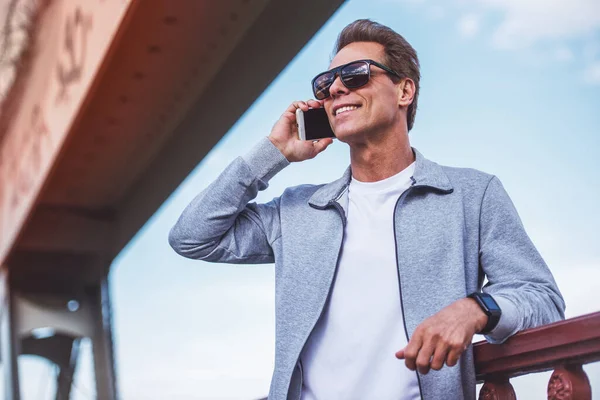 スポーツ制服とメガネでハンサムな中年の男が携帯電話で話しているし 朝のジョギング中に休憩しながら笑みを浮かべて — ストック写真