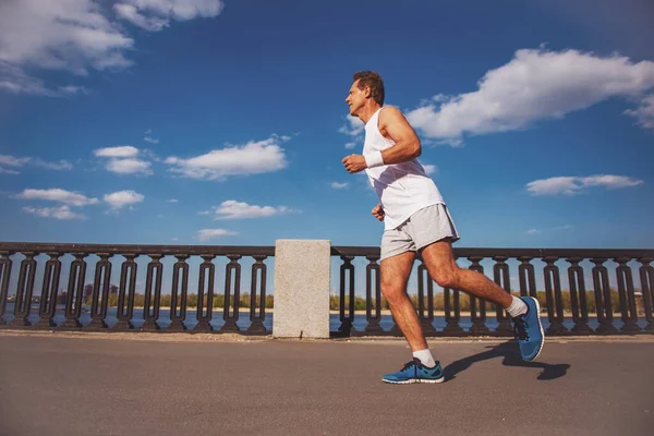 Stock image Side view of handsome middle aged man in sports uniform running on the bridge