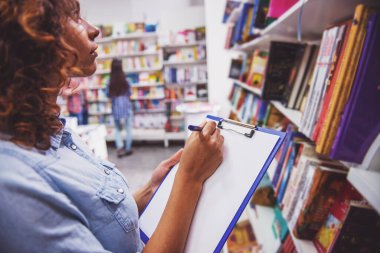 Kitapçıda bir kitap seçerken bir klasör tutan ve notlar yapma güzel Afro Amerikalı kız Kırpılmış görüntü