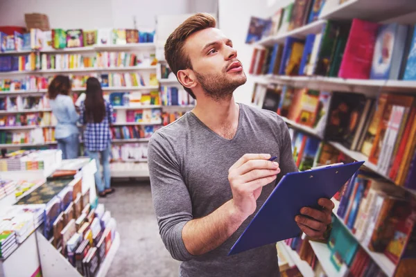 Handsome Young Man Holding Folder Making Notes While Choosing Book — Stock Photo, Image