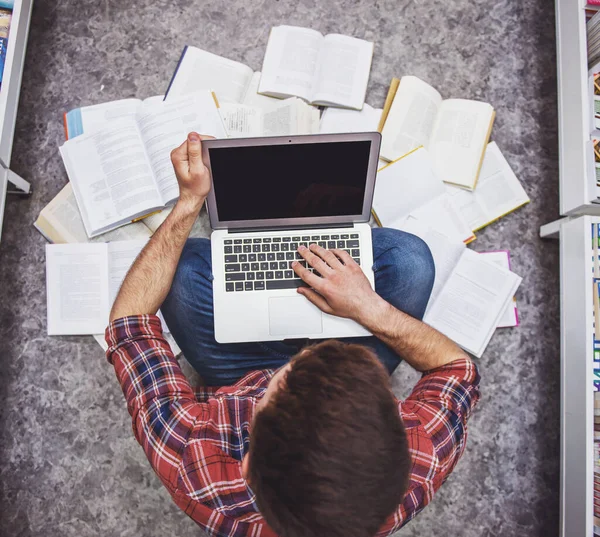 書店で開かれた本の中で床に座りながらノートパソコンを使って勉強するハンサムな学生のトップビュー — ストック写真