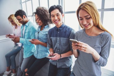 Gençler akıllı telefonlar kullanarak ve üst üste otururken gülümseyen farklı milletlerden