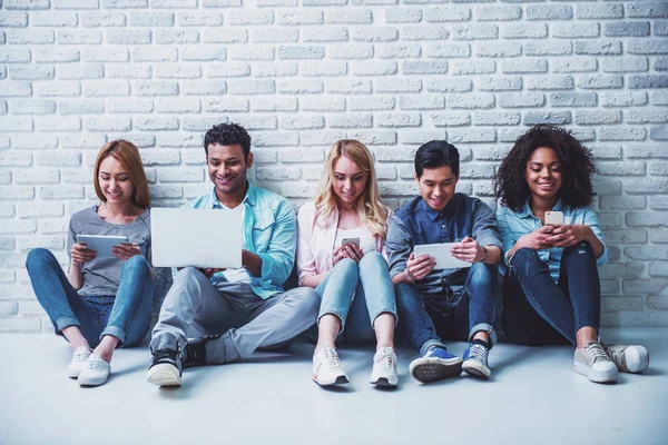 Hermosos Jóvenes Diferentes Nacionalidades Están Utilizando Gadgets Sonriendo Sentados Contra — Foto de Stock