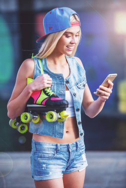 Güzel sarışın kız şapkalı bir cep telefonu kullanarak ve skate Park onun silindirleriyle ayakta gülümseyen