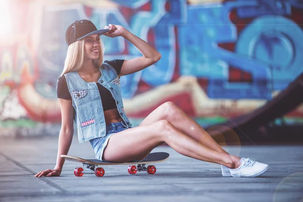 모자에 여자는 스케이트 공원에서 그녀의 스케이트 보드에 앉아있는 찾으십시오 — 스톡 사진
