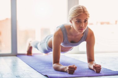 Spor giymiş güzel bir kadın yoga minderinde tahta egzersizi yapıyor.