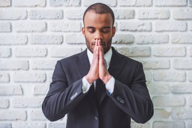 Yakışıklı Afro Amerikalı işadamı Klasik takım elbise eller birlikte dua gibi beyaz tuğla duvara tutuyor